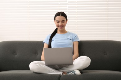 Photo of Happy woman working with laptop on sofa indoors