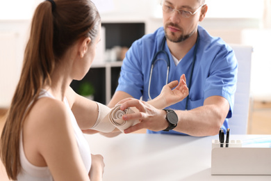 Photo of Male orthopedist applying bandage onto patient's elbow in clinic