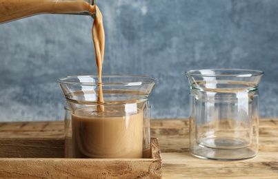 Photo of Pouring tasty coffee into glass cup on wooden table