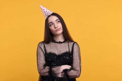 Sad woman in party hat on orange background