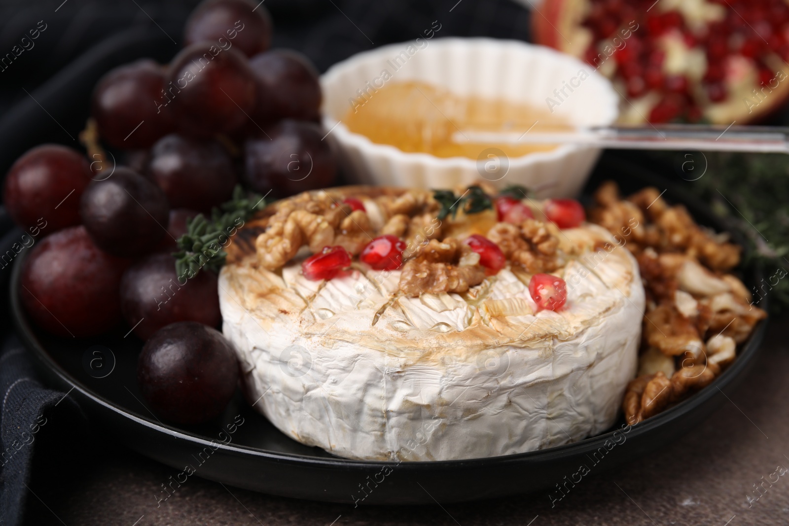 Photo of Plate with tasty baked camembert, honey, grapes, walnuts and pomegranate seeds on table, closeup