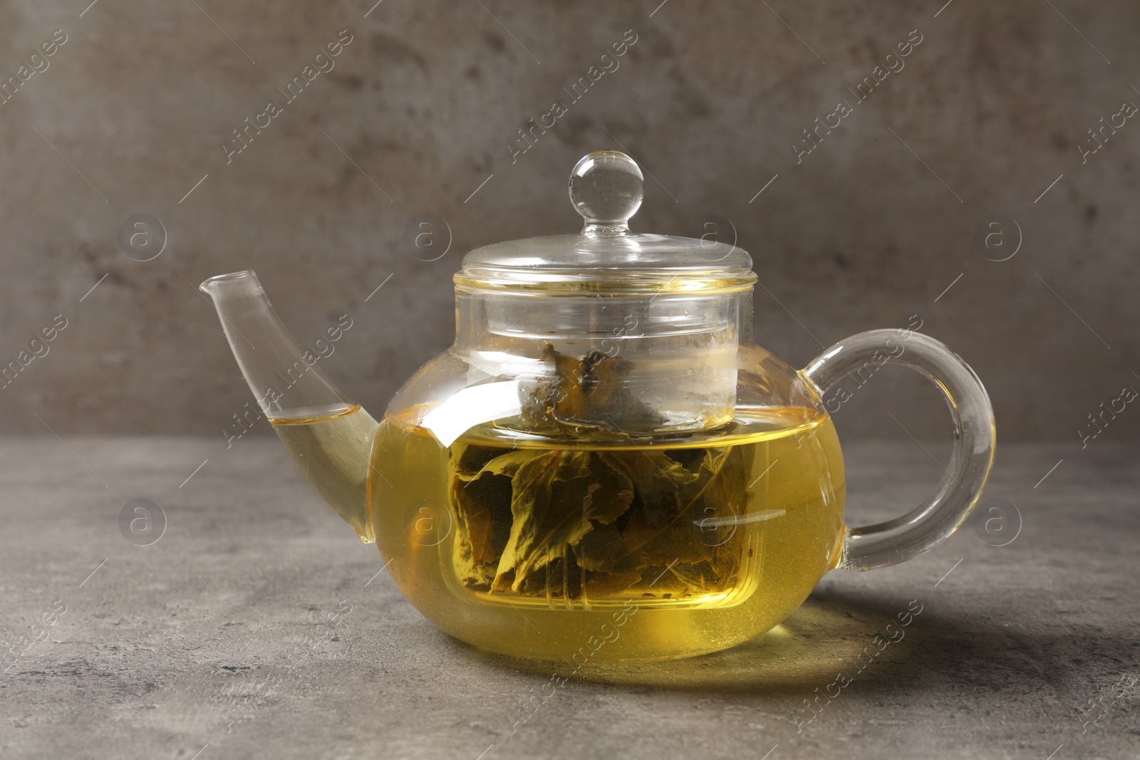 Photo of Glass teapot with oolong on table against grey background