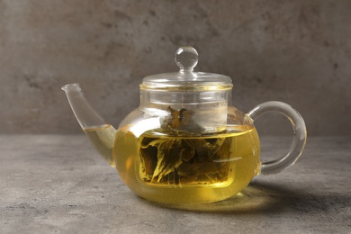 Photo of Glass teapot with oolong on table against grey background