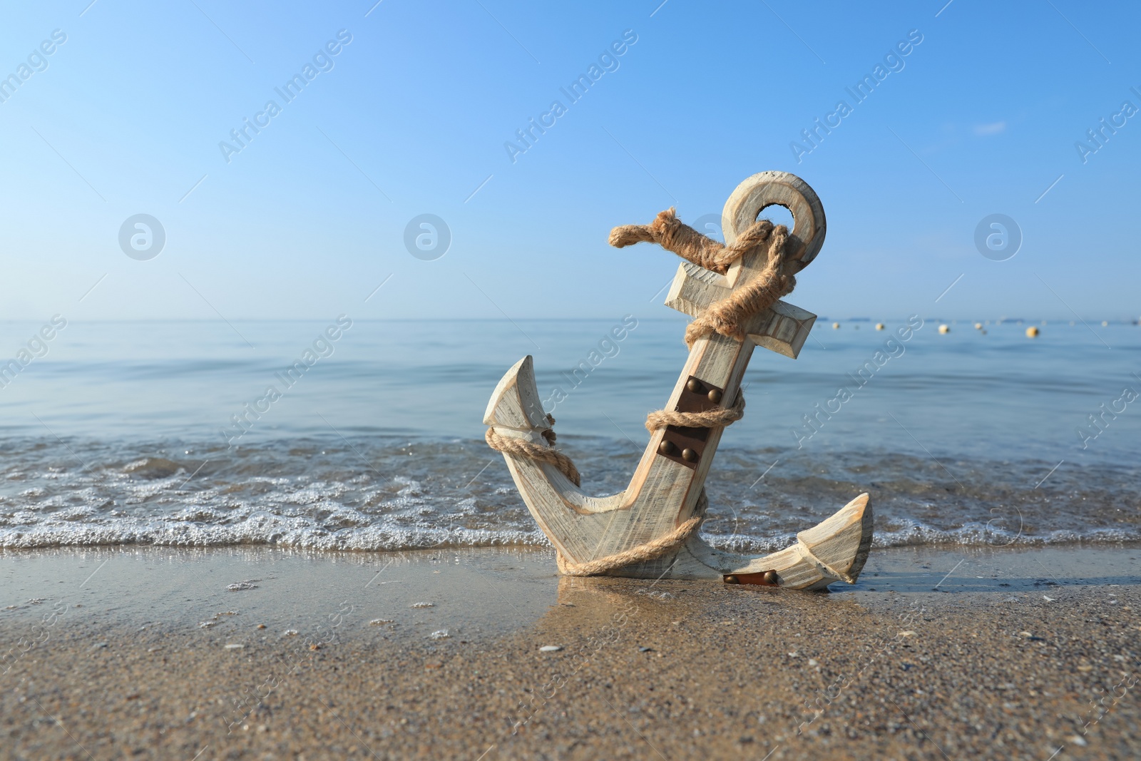 Photo of Wooden anchor with rope on sand near sea. Space for text