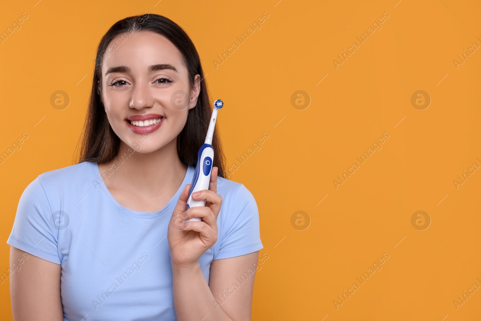 Photo of Happy young woman holding electric toothbrush on yellow background, space for text