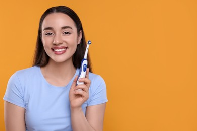 Happy young woman holding electric toothbrush on yellow background, space for text