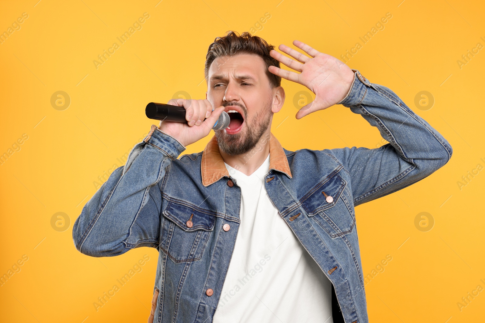 Photo of Handsome man with microphone singing on yellow background