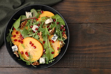 Photo of Tasty salad with persimmon, blue cheese, pomegranate and walnuts served on wooden table, top view. Space for text