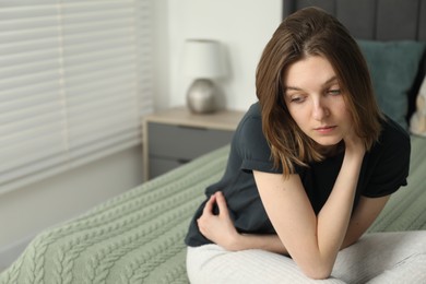 Photo of Sad young woman sitting on bed at home, space for text