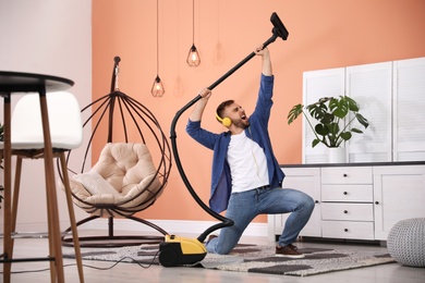 Photo of Young man having fun while vacuuming at home