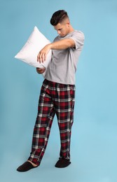 Photo of Somnambulist with soft pillow on light blue background. Sleepwalking