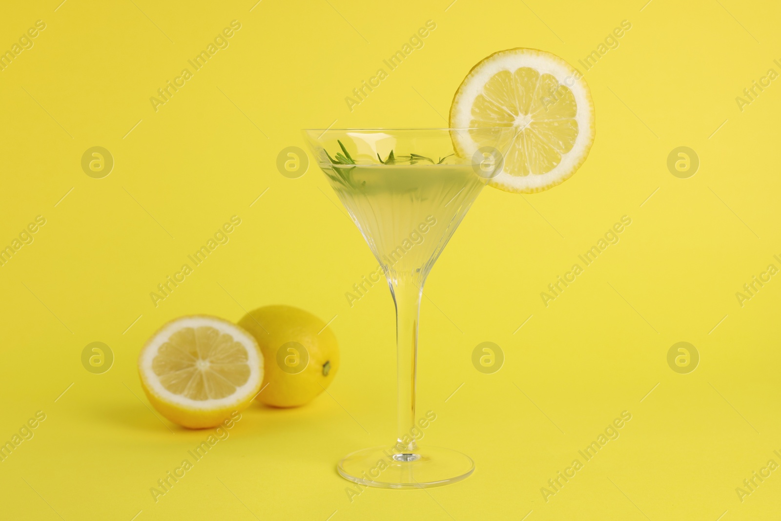 Photo of Martini glass of refreshing cocktail with lemon slice, rosemary and fruits on yellow background