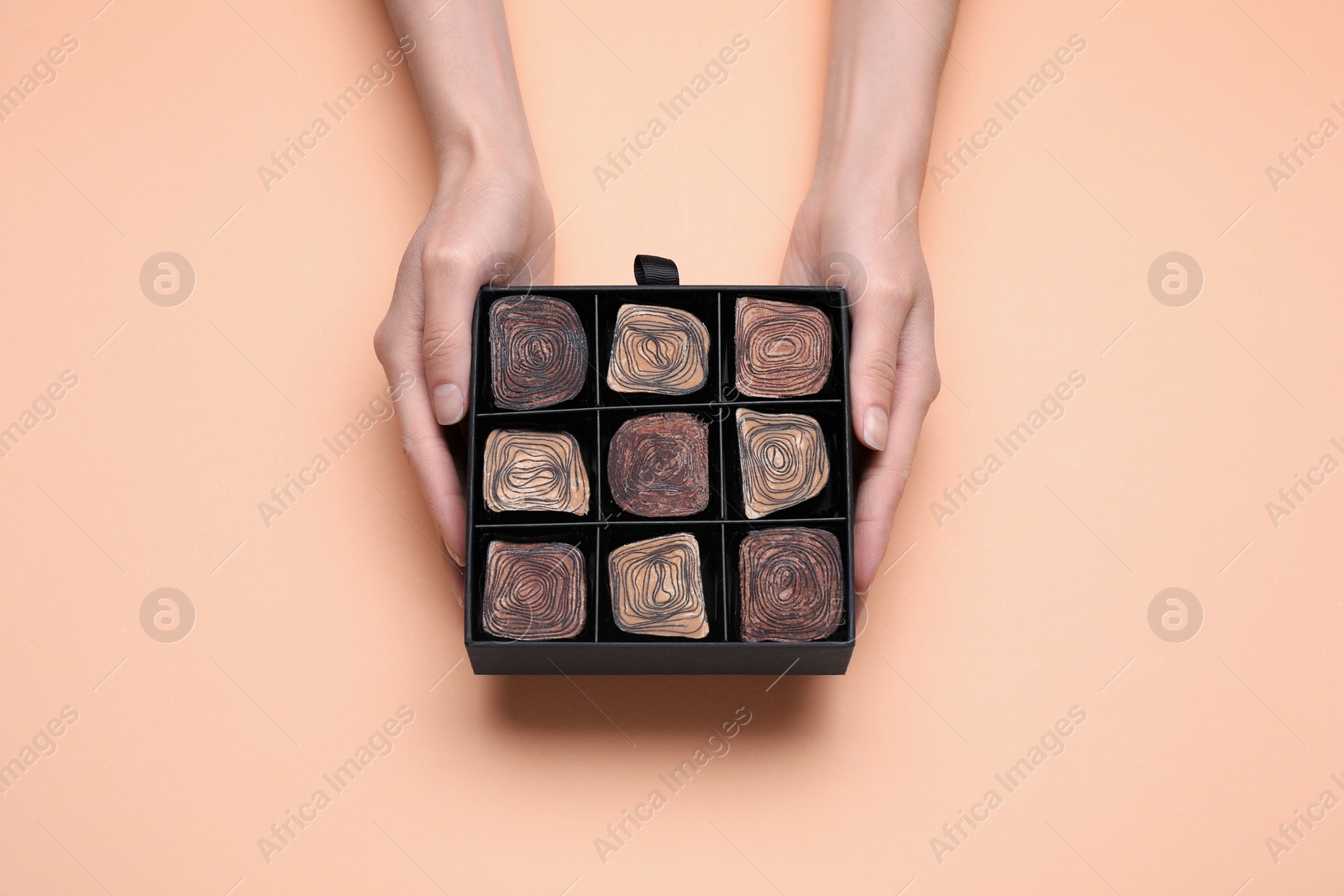 Photo of Woman with box of delicious chocolate candies on beige background, top view