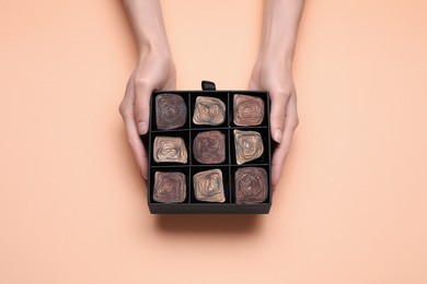 Woman with box of delicious chocolate candies on beige background, top view