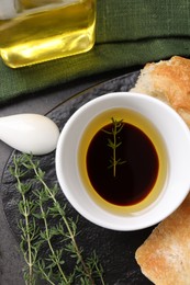 Photo of Bowl of organic balsamic vinegar with oil, thyme and bread on grey table, flat lay