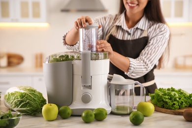 Photo of Young woman making tasty fresh juice at table in kitchen, closeup