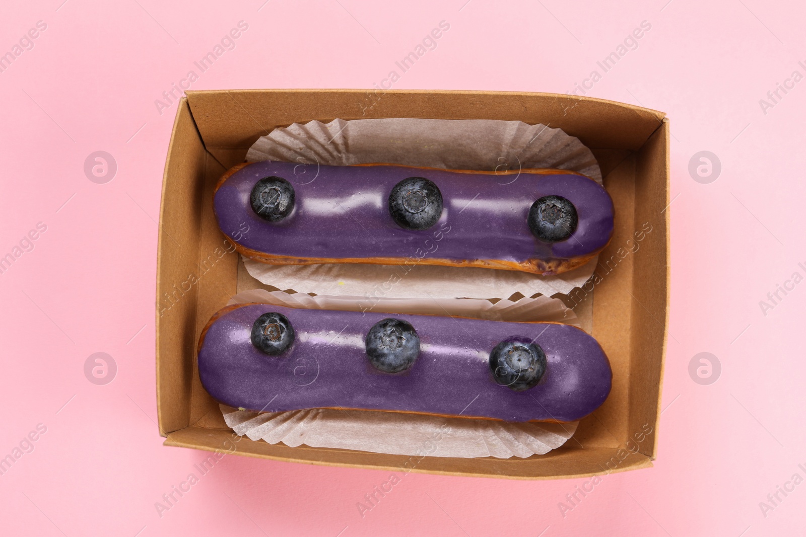 Photo of Delicious eclairs decorated with blueberries on pink background, top view