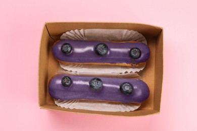 Photo of Delicious eclairs decorated with blueberries on pink background, top view