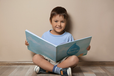 Photo of Cute little boy reading book on floor near beige wall