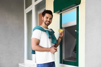 Photo of Young man with credit card near cash machine outdoors