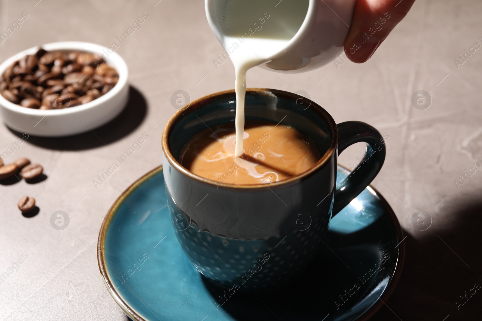 Photo of Woman pouring milk into cup with aromatic coffee at light table, closeup