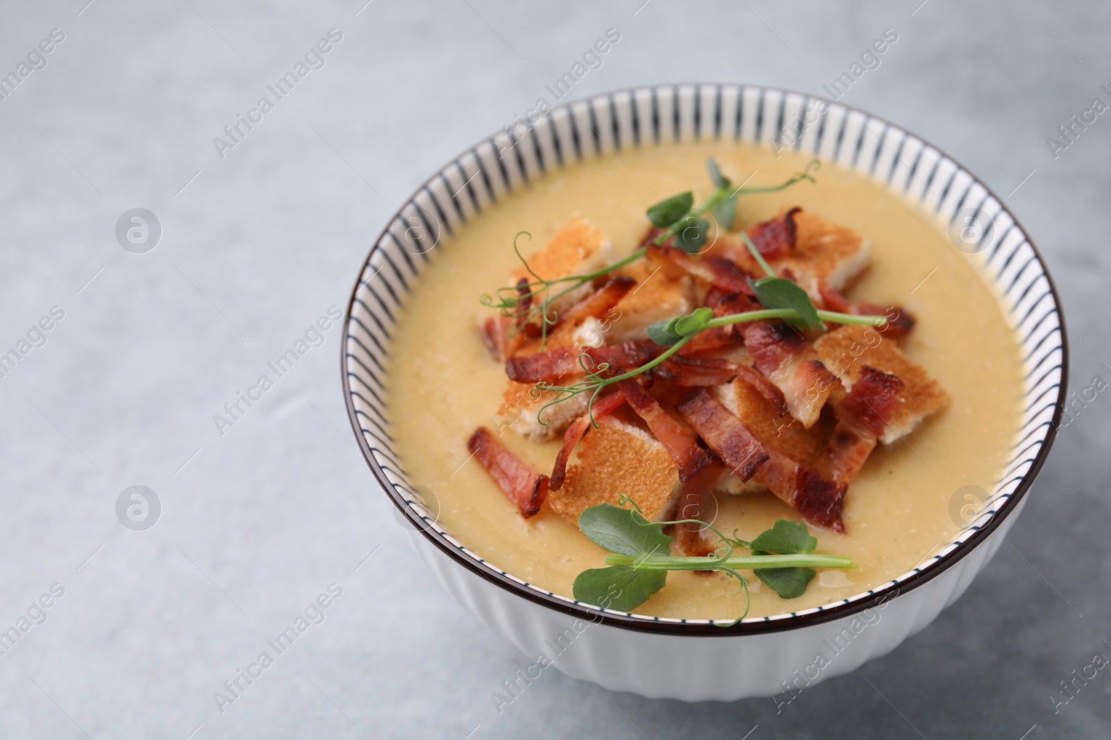 Photo of Delicious lentil soup with bacon and microgreens in bowl on gray table, closeup. Space for text