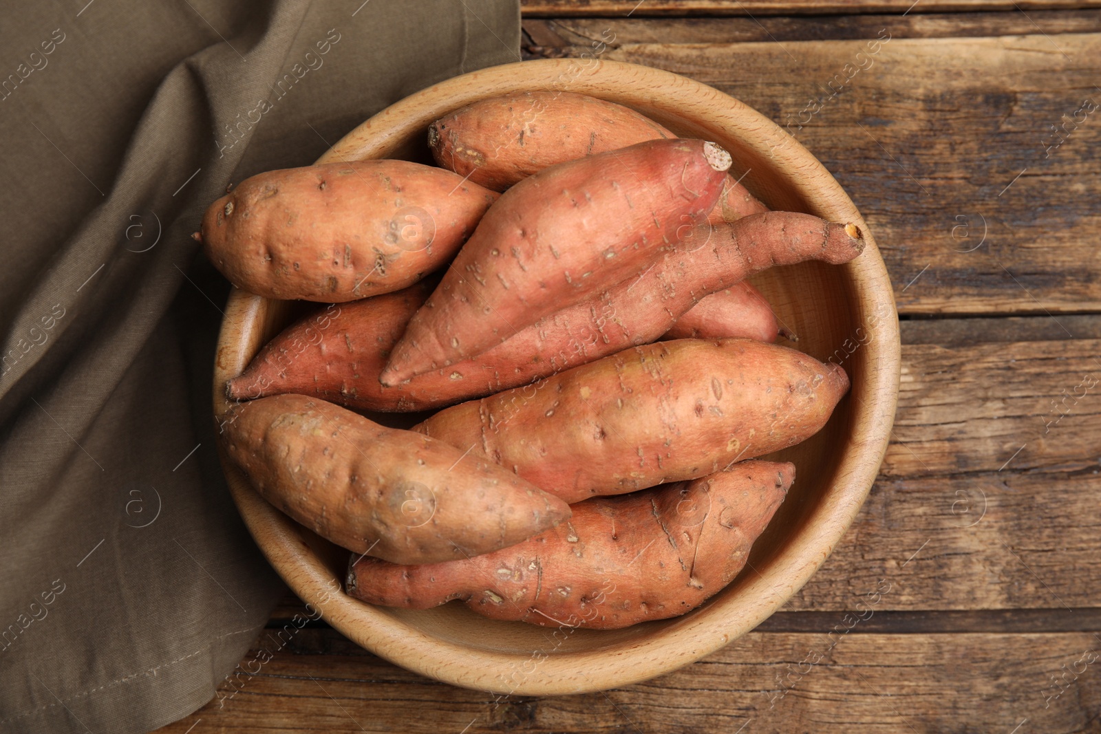 Photo of Fresh whole sweet potatoes in bowl on wooden table, top view