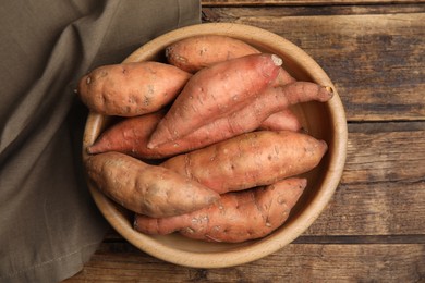 Photo of Fresh whole sweet potatoes in bowl on wooden table, top view