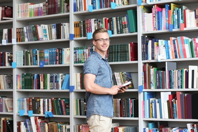 Photo of Young man with book near shelving unit in library