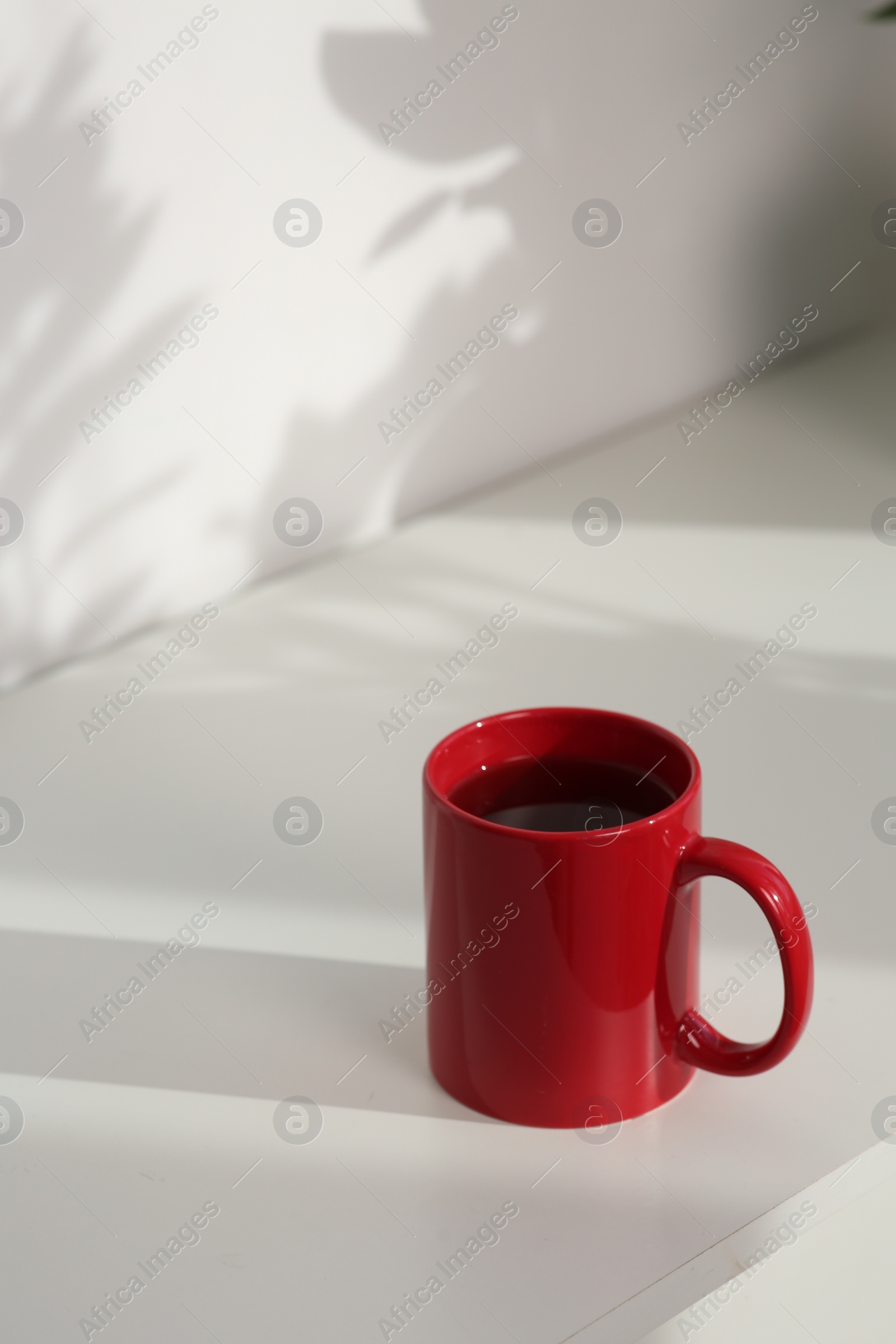 Photo of Red ceramic mug with drink on white table indoors. Mockup for design