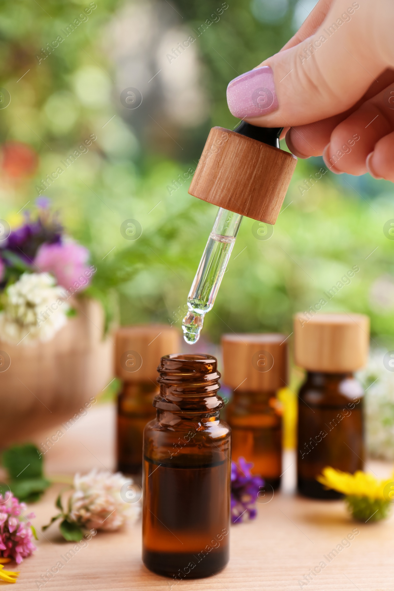 Photo of Woman dripping essential oil into bottle at wooden table, closeup