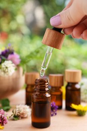 Woman dripping essential oil into bottle at wooden table, closeup