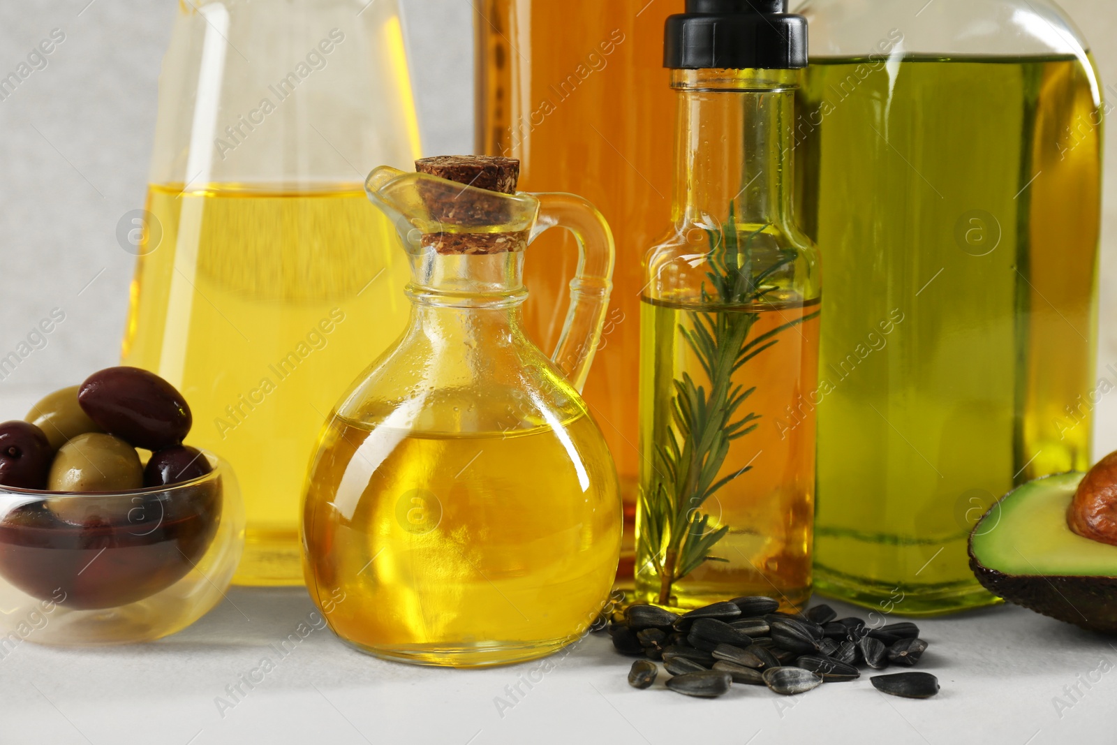 Photo of Vegetable fats. Different cooking oils in glass bottles and ingredients on white table, closeup