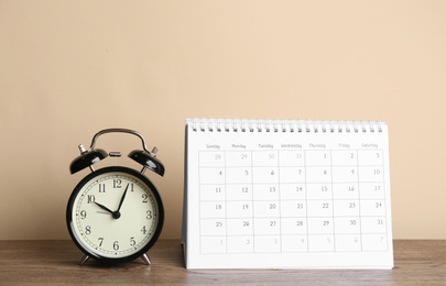 Calendar and alarm clock on wooden table against beige background