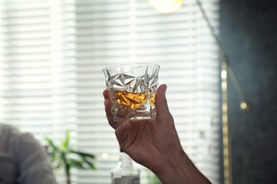 Man with glass of whiskey indoors, closeup view