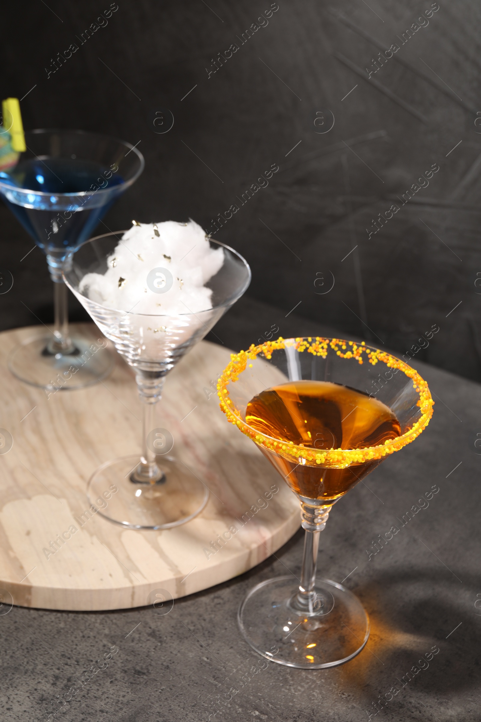 Photo of Tasty cotton candy cocktail and other alcoholic drinks in glasses on gray textured table