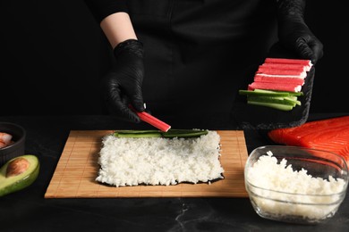 Photo of Chef in gloves making sushi roll at dark table, closeup