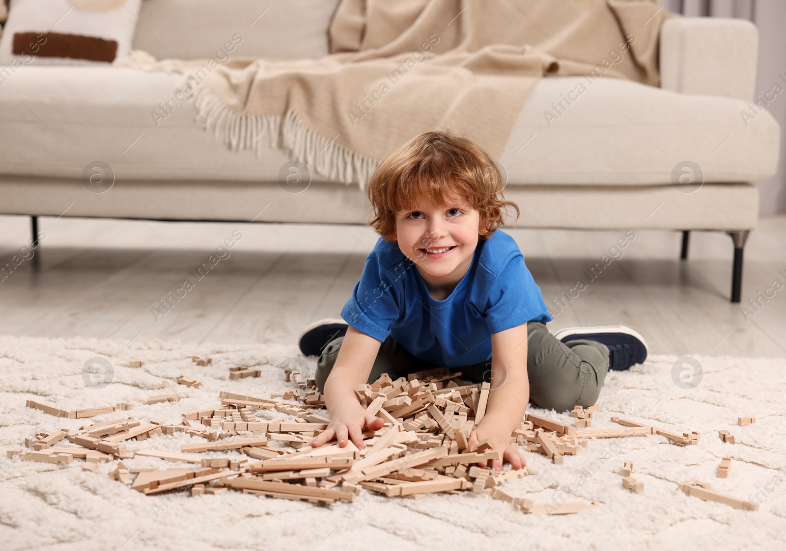 Photo of Cute little boy playing with wooden construction set on carpet at home. Child's toy