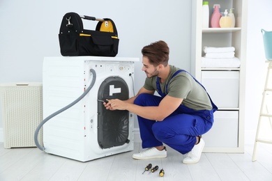 Photo of Young handyman fixing washing machine at home. Laundry day