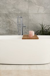 Photo of Stylish white tub and wooden tray with candles in bathroom. Interior design