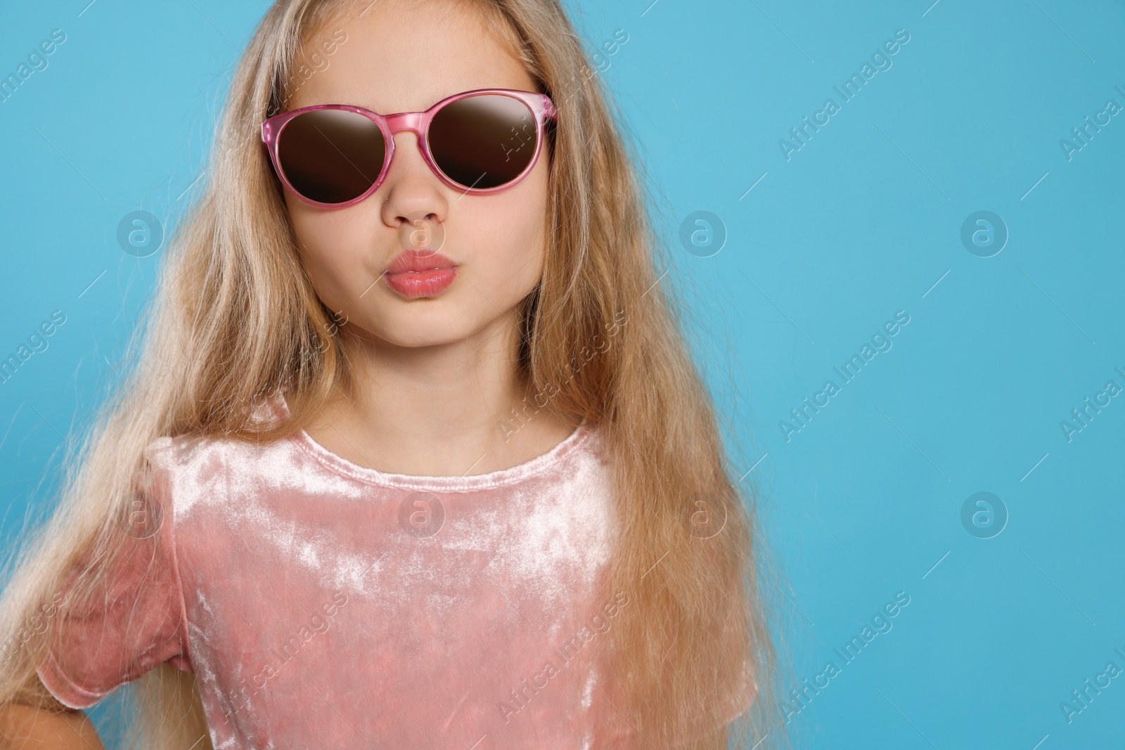 Photo of Girl in stylish sunglasses on light blue background. Space for text