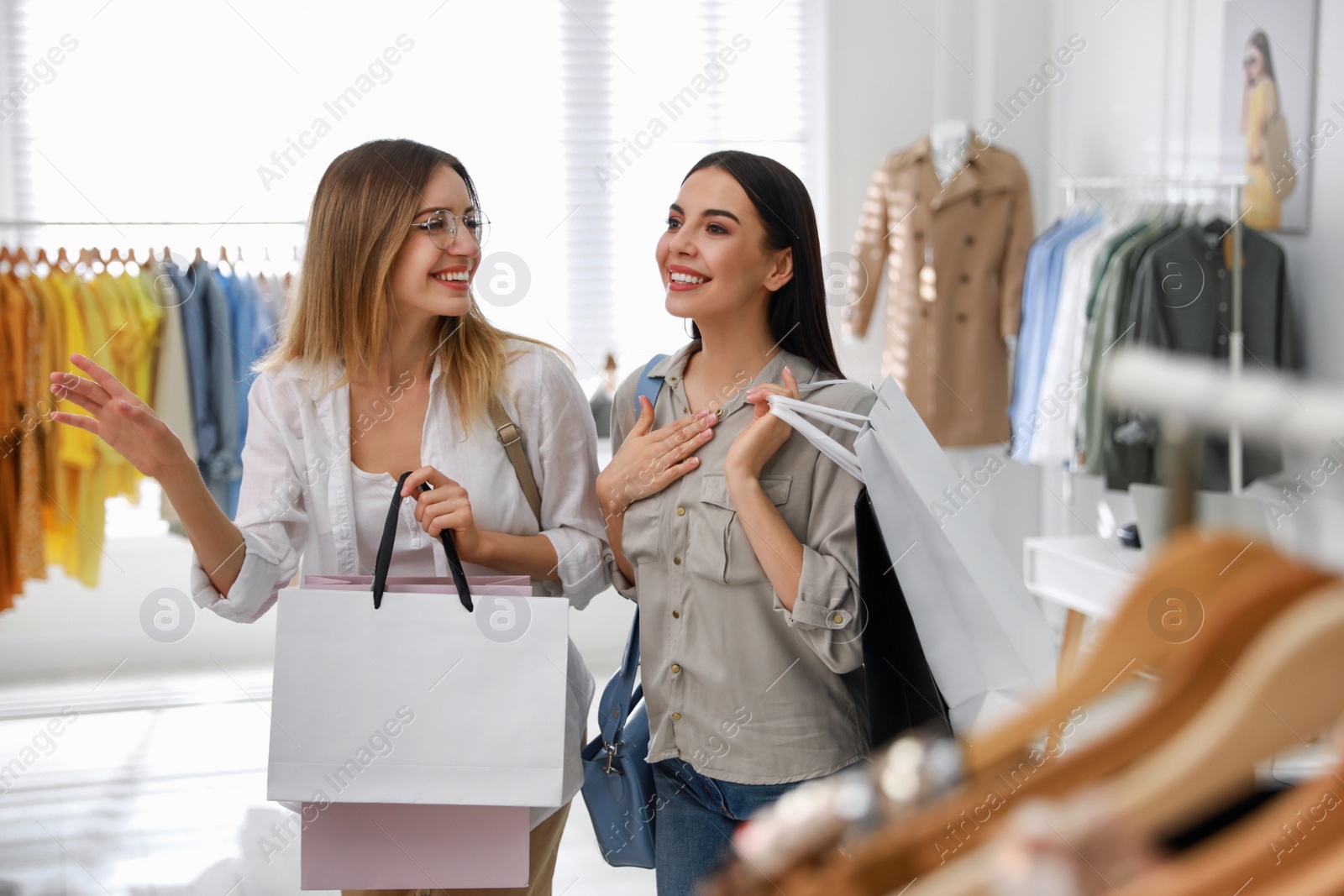 Photo of Young women with shopping bags choosing clothes in modern boutique