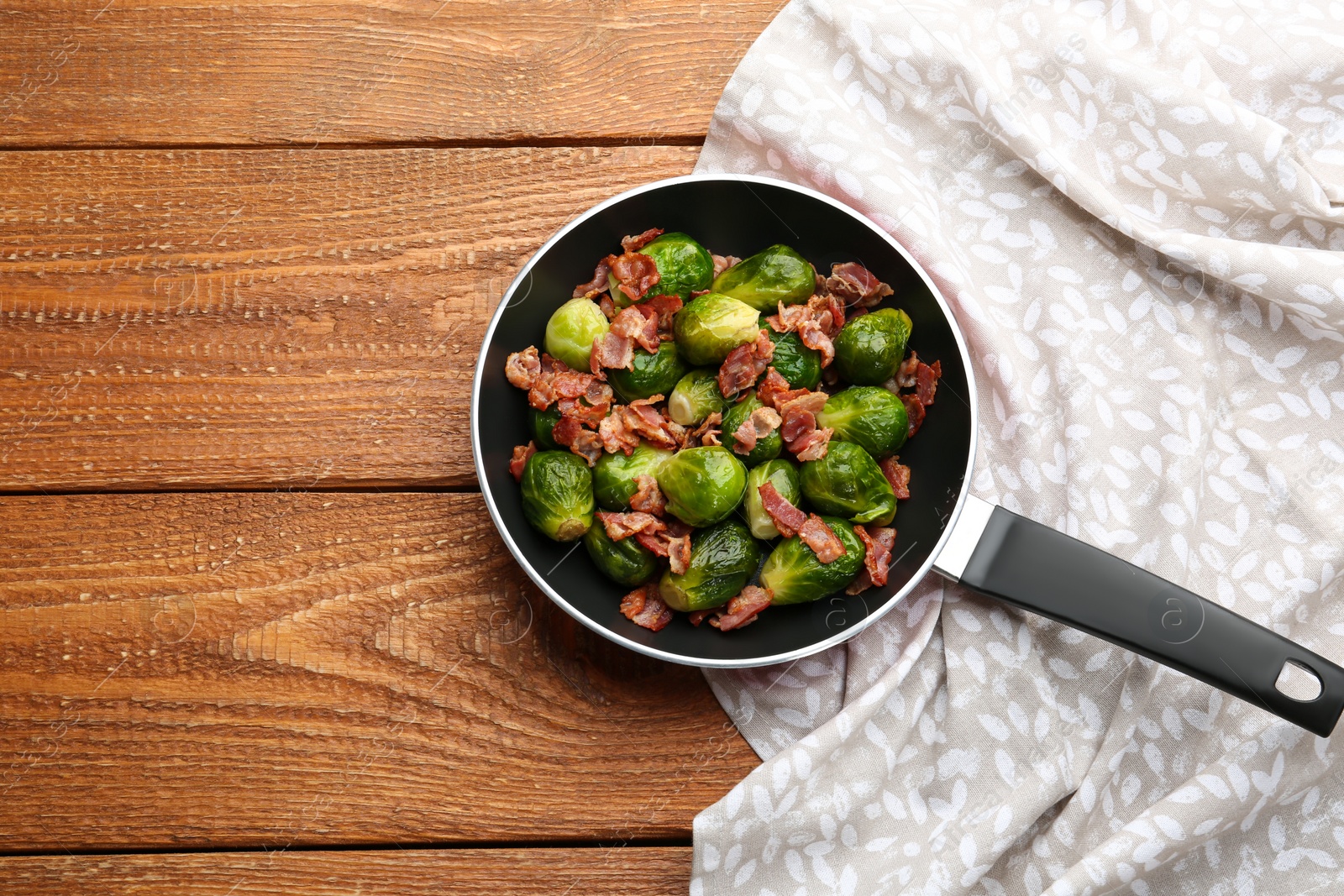 Photo of Tasty roasted Brussels sprouts with bacon on wooden table, top view. Space for text