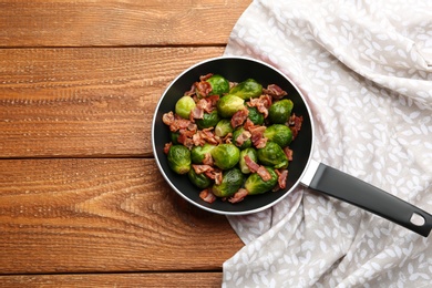 Tasty roasted Brussels sprouts with bacon on wooden table, top view. Space for text