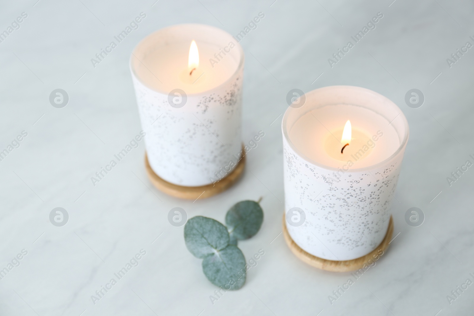 Photo of Burning candles in holders and beautiful eucalyptus branch on grey table, closeup. Interior element