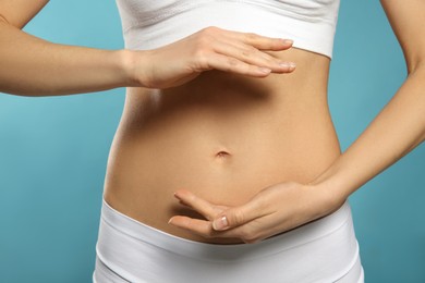 Photo of Woman holding hands near belly against light blue background, closeup