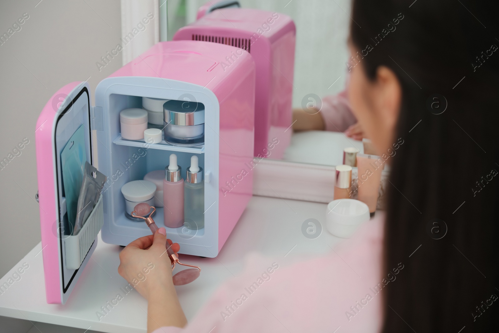 Photo of Woman taking face roller out of cosmetic refrigerator indoors, closeup