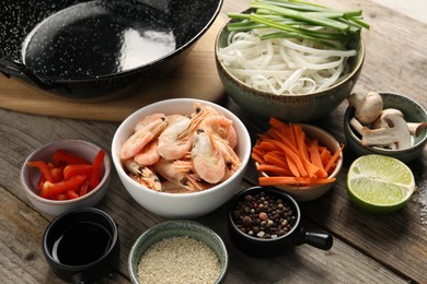 Different products and black wok on wooden table, closeup