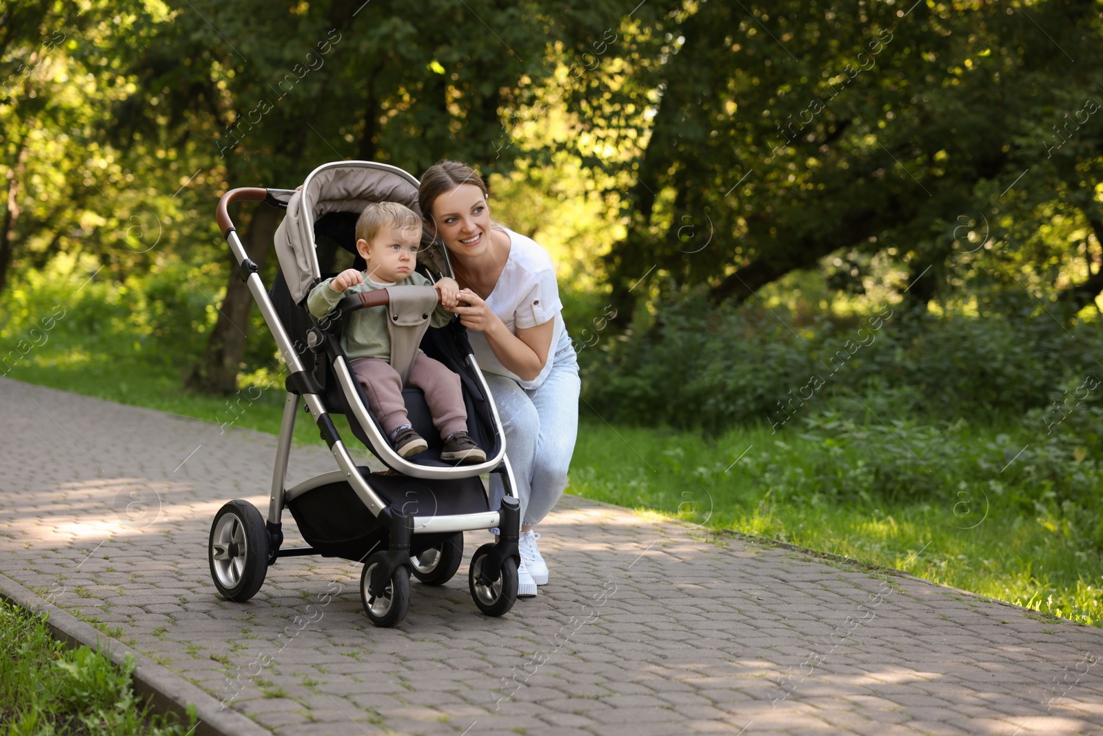 Photo of Happy nanny and cute little boy in stroller in park, space for text