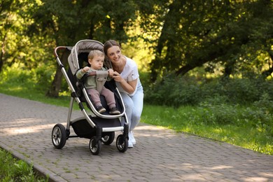 Happy nanny and cute little boy in stroller in park, space for text